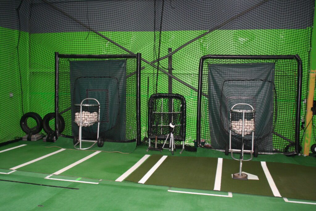A green wall with two batting cages and one is empty.