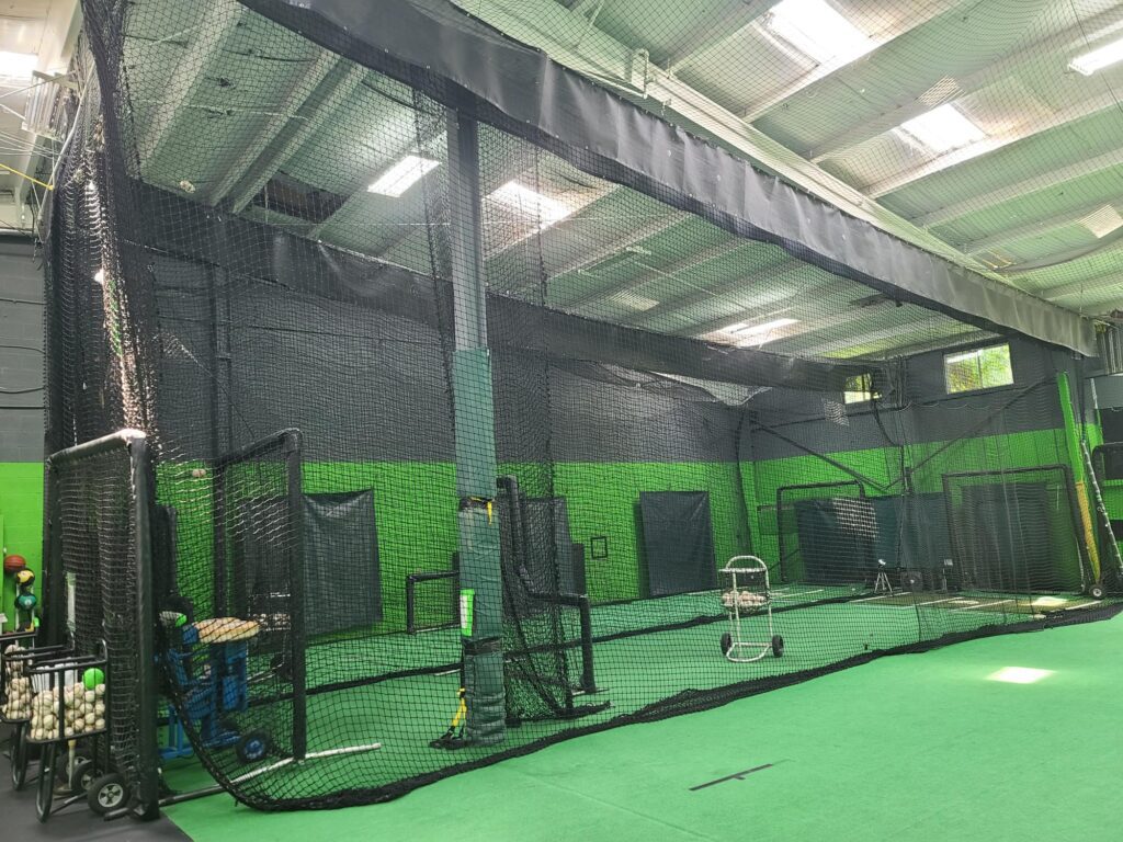 A large indoor batting cage with green walls.