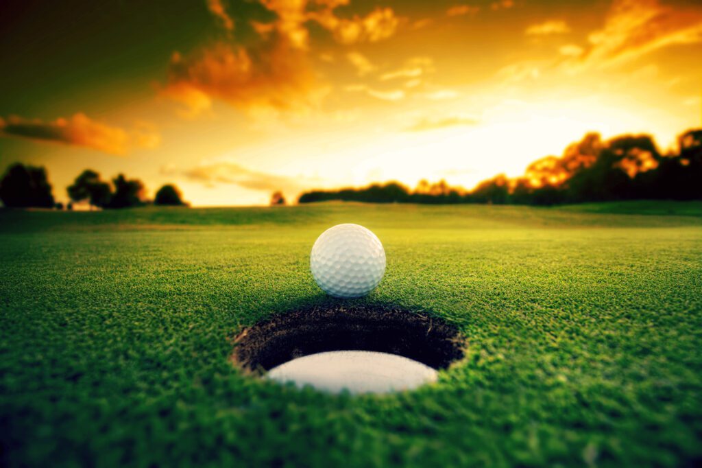 A golf ball is in the hole at sunset.